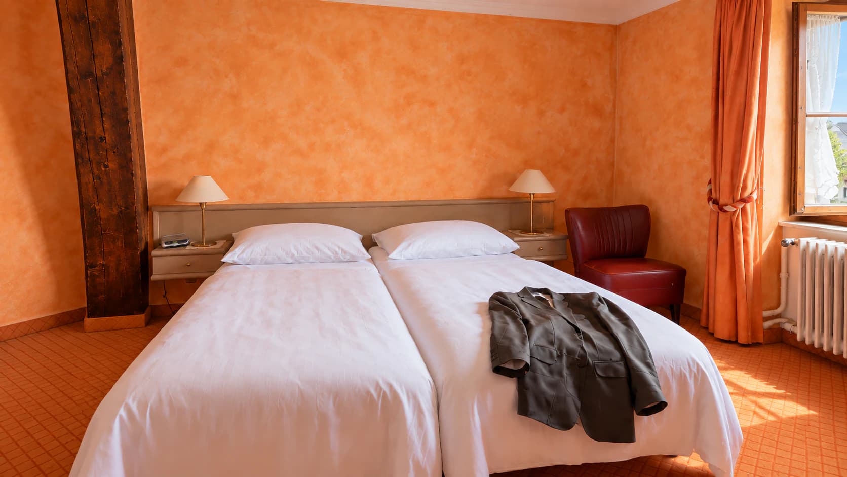 Lits jumeaux, lampes de chevet et poutre apparente dans une chambre aux murs orangés